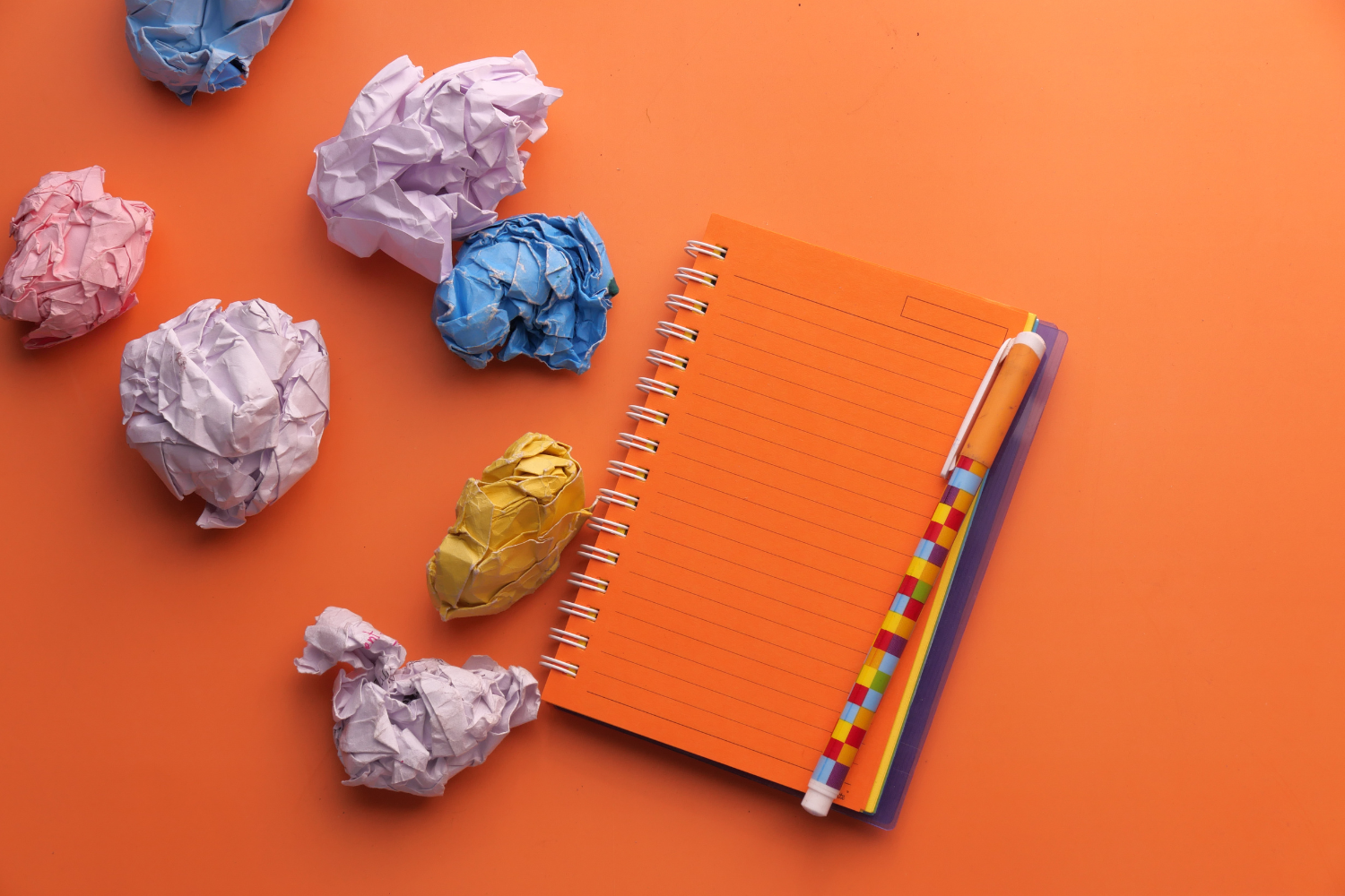 tipologie di brand name - nell'immagine, a rappresentare il processo di progettazione del naming, un quaderno arancione, una penna e diversi fogli accartocciati che simboleggiano i tentativi di trovare il giusto nome per un brand o un progetto